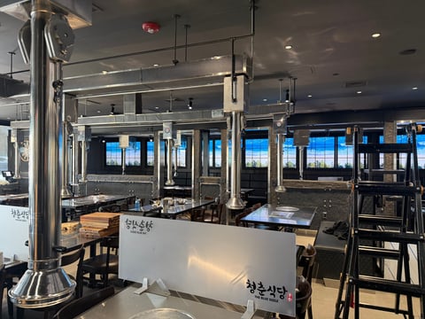 Modern Asian restaurant interior with white counter seating, black bar stools, and blue-tinted windows overlooking a skyline